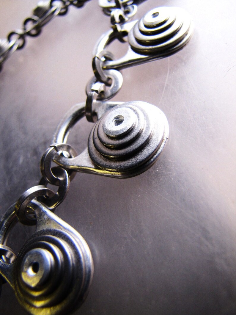 May include: A silver chain bracelet with multiple circular charms. Each charm is made of stacked metal rings, creating a layered effect.