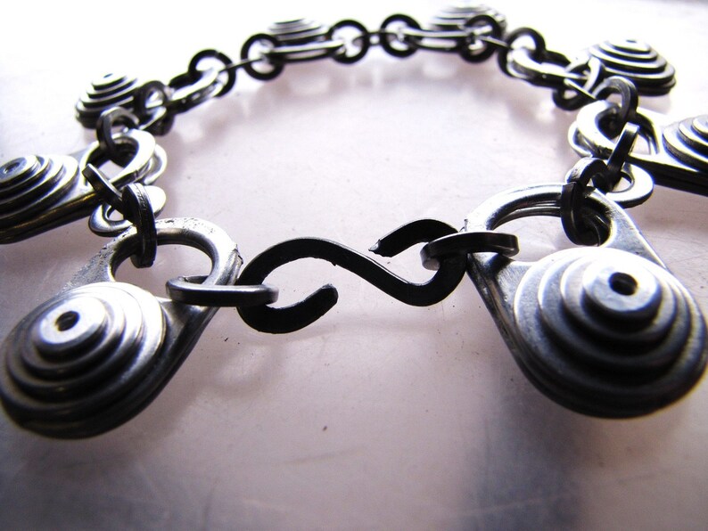 May include: A silver bracelet made from stacked metal rings connected by a black chain. The bracelet has a black metal clasp.