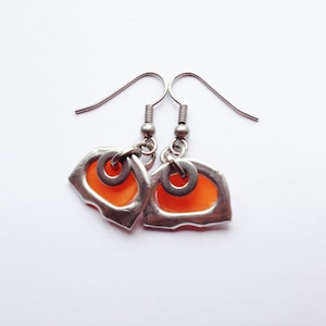 May include: A pair of silver earrings with orange glass accents. The earrings have a unique, abstract shape and are suspended from silver hooks.