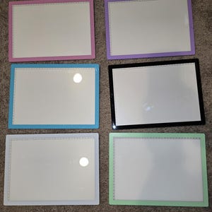 Może przedstawiać: Sześć podkładek świetlnych z białymi powierzchniami i różnokolorowymi ramkami. Ramki są różowe, fioletowe, niebieskie, czarne, białe i zielone.