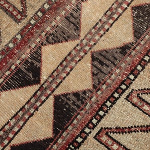 Könnte beinhalten: Nahaufnahme eines beige-braunen Teppichs mit geometrischen Mustern. Der Teppich weist ein sich wiederholendes Zickzackmuster in Rot und Schwarz mit einer zentralen Raute auf. Der Teppich hat einen Used-Look.