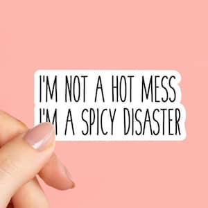 May include: A white sticker with black text that reads "I'M NOT A HOT MESS I'M A SPICY DISASTER." The sticker is held by a hand against a pink background. The text is in a simple sans-serif font.