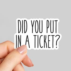 May include: A white sticker with black text that reads "DID YOU PUT IN A TICKET?" The sticker is held by a hand with a light gray background.