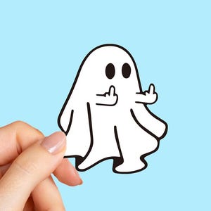 May include: A white ghost cartoon sticker with black eyes and outline, giving the middle finger with both hands. The sticker is held against a light blue background.