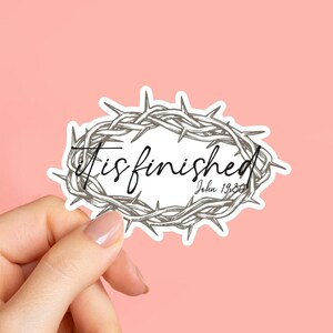 May include: A sticker featuring a gray, hand-drawn illustration of a crown of thorns encircling the words "It is finished" and the Bible verse John 19:30. The sticker is on a pink background.
