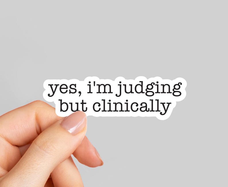 May include: A white sticker with black text that reads "yes, I'm judging but clinically." The sticker is held by a hand with a light gray background.