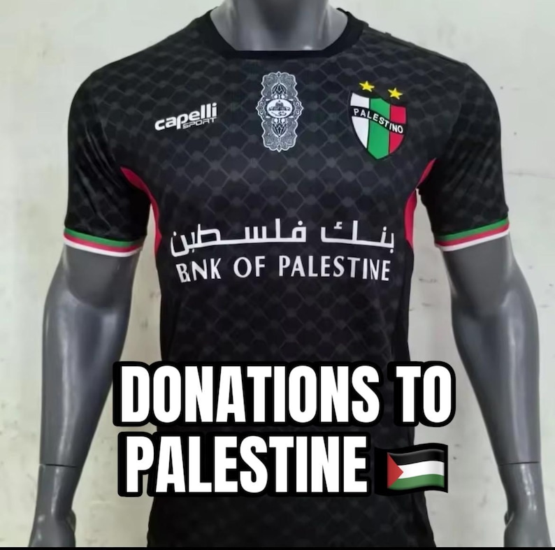 May include: Black soccer jersey with a green, white, and red logo that says "Palestino" and two gold stars. The jersey also has the text "Bank of Palestine" in Arabic and English. The jersey is on a mannequin and has the text "Donations to Palestine" and a Palestinian flag.