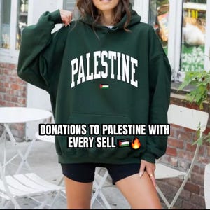 Puede incluir: Sudadera con capucha verde oscuro con la palabra "PALESTINE" en letras blancas. La sudadera con capucha tiene un bolsillo delantero y una capucha. El texto "DONATIONS TO PALESTINE WITH EVERY SELL" se muestra debajo.