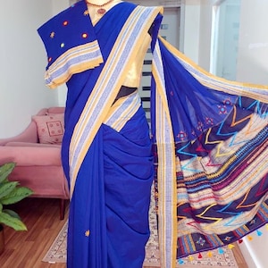 May include: A vibrant blue saree with embroidered details and a contrasting border. The saree is draped on a mannequin, showcasing its intricate design and flowing fabric. The border features yellow and white stripes. The saree is a traditional garment.
