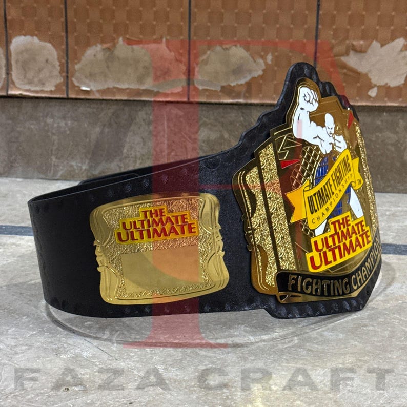 May include: A black and gold championship belt with the text "THE ULTIMATE ULTIMATE FIGHTING CHAMPIONSHIP" on the front. The belt has a gold buckle and a black leather strap. The belt is designed for a fighting competition.