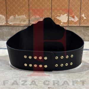 May include: Black leather championship belt with gold-colored studs. The belt has a curved shape and a large, decorative top. The text "FAZA CRAFT" is visible at the bottom of the image.