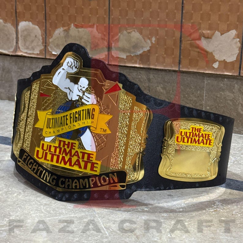 May include: A gold and black Ultimate Fighting Championship belt. The belt features gold plates with the text "Ultimate Fighting Championship" and "The Ultimate Fighting Champion". The belt is made of black leather.
