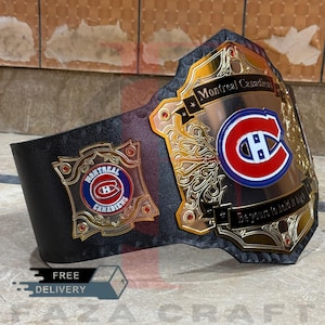 May include: A black and gold championship belt with the Montreal Canadiens logo. The belt features a large central emblem with the team's logo and the words "Montreal Canadiens". The text "Be yours to hold it high" is also visible.