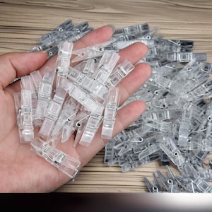 May include: A large quantity of clear plastic clothespins with metal springs. The clothespins are small and have a rectangular shape.