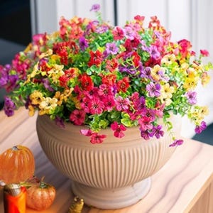 May include: A brown ceramic planter with a textured surface holds a bouquet of colorful artificial flowers. The flowers are a mix of pink, red, yellow, and purple.
