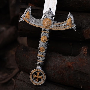 May include: An ornate sword with a silver blade and a detailed handle. The handle features gold and silver accents, with a cross-shaped design at the pommel. The hilt has intricate carvings and a decorative crossguard.