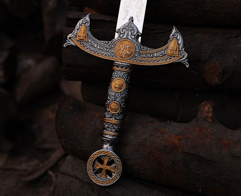 May include: An ornate sword with a silver blade and a detailed handle. The handle features gold and silver accents, with a cross-shaped design at the pommel. The hilt has intricate carvings and a decorative crossguard.