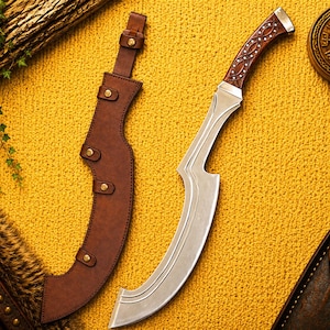 Puede incluir: Una hoja de metal curva con acabado plateado pulido y un mango de madera marrón con intrincados patrones de incrustaciones de plata, acompañada de una funda de cuero marrón a juego asegurada con cuatro remaches de metal y una correa.