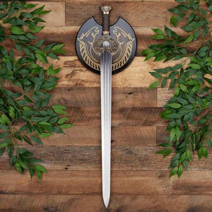 May include: A double-edged steel sword with a central fuller, featuring an ornate bronze-toned hilt with intricate scrollwork. The sword is mounted on a circular black wooden plaque decorated with gold-colored line art of two horse heads.