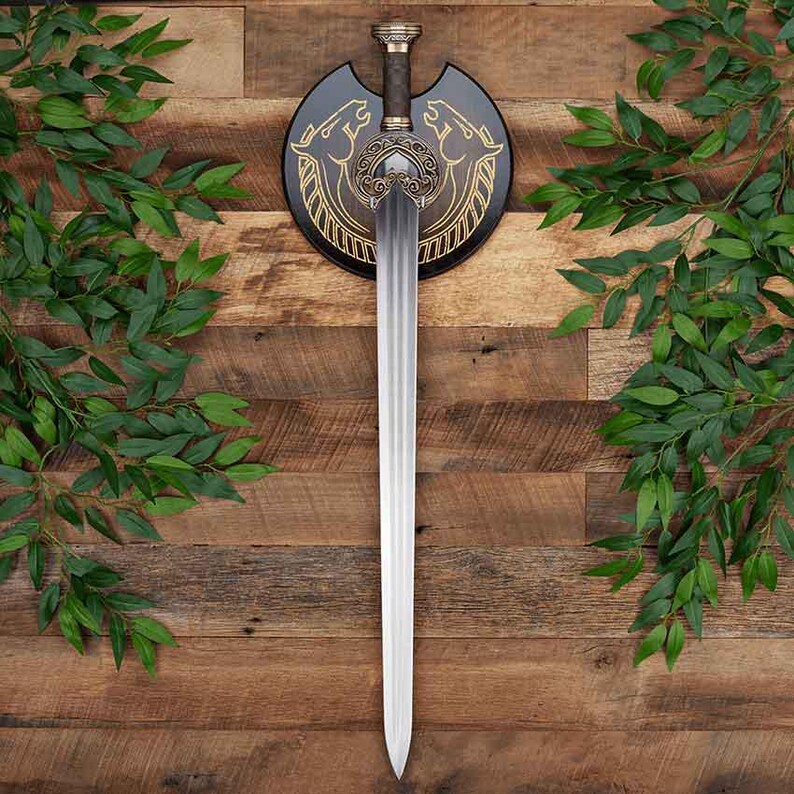 May include: A double-edged steel sword with a central fuller, featuring an ornate bronze-toned hilt with intricate scrollwork. The sword is mounted on a circular black wooden plaque decorated with gold-colored line art of two horse heads.