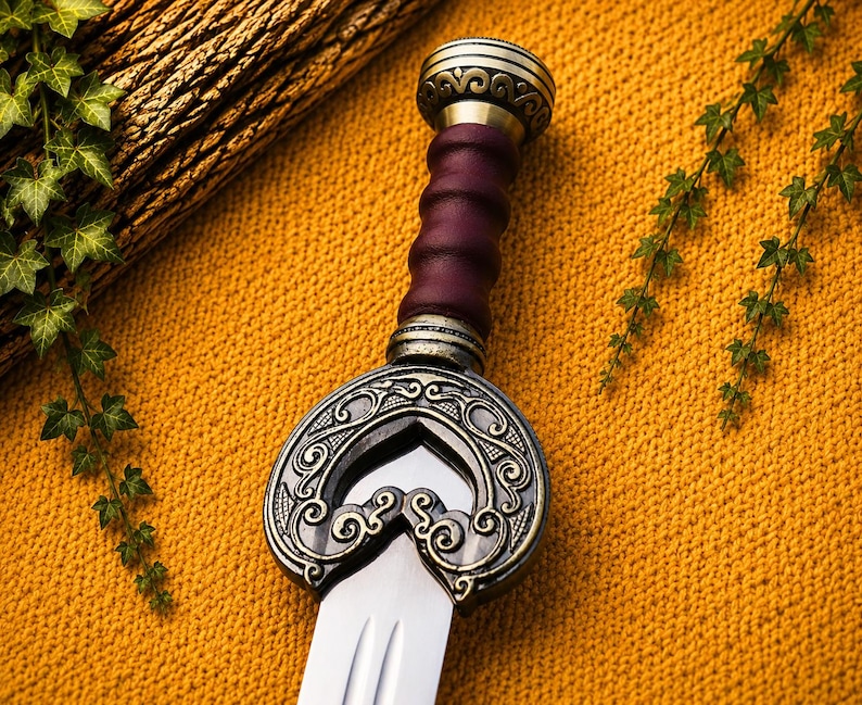 May include: A sword with a polished steel blade and a dark purple, ribbed leather grip. The hilt features an ornate, antiqued brass crossguard with intricate swirling patterns and a matching brass pommel at the top of the handle.
