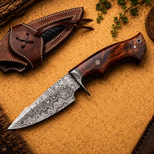 May include: A fixed-blade knife with a patterned Damascus steel blade and a polished dark brown wooden handle. The knife features a metal bolster and a lanyard hole. It is accompanied by a brown leather sheath with visible stitching and a leather tie.