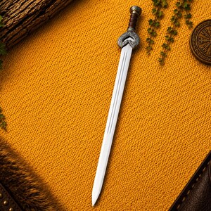 May include: A double-edged sword with a silver-toned blade and a central fuller. The hilt features an ornate, heart-shaped silver crossguard with intricate scrollwork, a dark brown leather-wrapped grip, and a cylindrical silver pommel.