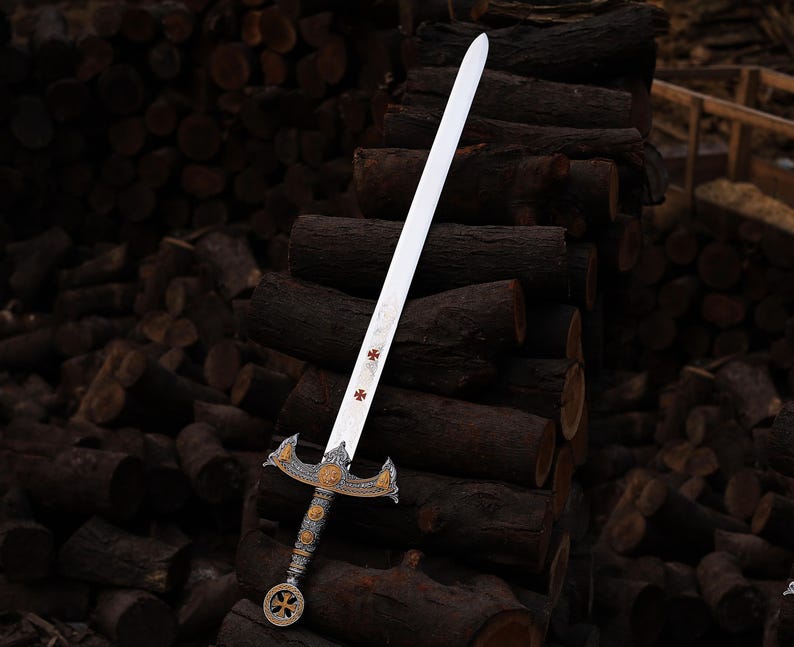 May include: A decorative sword with a silver blade and ornate gold and silver hilt. The blade features red cross symbols. The sword is displayed against a backdrop of stacked logs, showcasing its historical design.