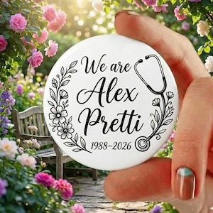 Pode incluir: Um botão circular branco com o texto "We are Alex Pretti 1988-2026" em escrita preta, rodeado por ilustrações florais e um estetoscópio. O botão é segurado em uma mão contra um fundo de flores e um banco de madeira.