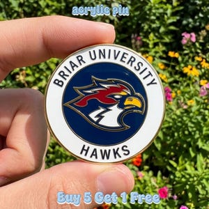 May include: Round acrylic pin featuring the Briar University Hawks logo. The pin has a white border with gold trim, surrounding a blue center with a red and yellow hawk emblem. The text "BRIAR UNIVERSITY" and "HAWKS" are displayed. The text "acrylic pin" is also visible.