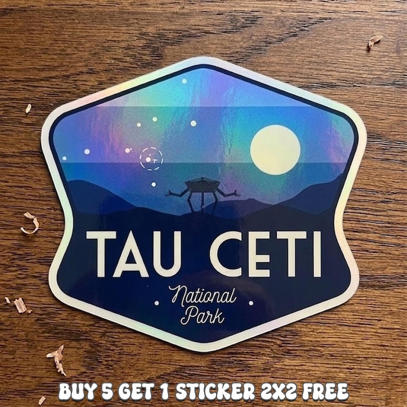 May include: A holographic sticker with a shield shape. The sticker features a night sky scene with a full moon, stars, and a silhouetted alien figure. The text "TAU CETI" and "National Park" are printed on the sticker.