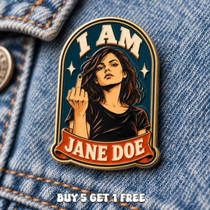 May include: A metal enamel pin featuring an illustration of a person with dark hair wearing a black shirt, gesturing with a middle finger. The text reads I AM JANE DOE in a gold-bordered arch. The pin has a dark blue background and orange banner.