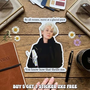 May include: A white sticker featuring a portrait of a woman with the text "By all means, move at a glacial pace" and "You know how that thrills me." The sticker is surrounded by stationery and flowers.