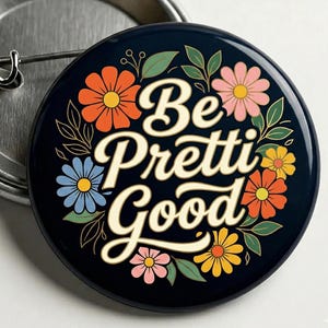 Pode incluir: Um botão redondo azul marinho com as palavras "Be Pretti Good" em uma fonte extravagante. O botão é decorado com flores coloridas em laranja, rosa, amarelo e azul, e folhas verdes.
