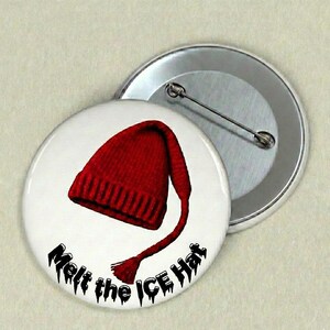 Może przedstawiać: Biała przypinka z grafiką czerwonej czapki i czarnym napisem "Melt the ICE Hat". Drugi, srebrny guzik jest częściowo widoczny w tle.