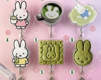 May include: Six acrylic badge reels featuring white rabbit characters and matcha-themed designs. Designs include a rabbit with a drink, a matcha latte with rabbit foam art, a rabbit on a green background, a rabbit with a cup, a square matcha cookie, and a rabbit-shaped cookie.