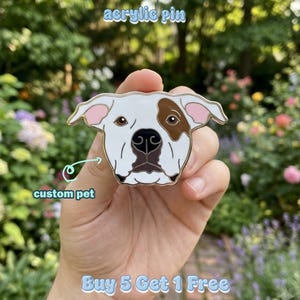 May include: An acrylic pin shaped like a dog head with white fur, a brown patch over the left eye, pink inner ears, and a black nose. The text "acrylic pin" appears at the top, "custom pet" with an arrow, and "Buy 5 Get 1 Free" at the bottom.