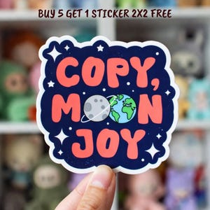 May include: A colorful sticker with the words "COPY, MOON, JOY" in red, with a moon and earth graphic. The sticker has a dark blue border with white stars. The text "BUY 5 GET 1 STICKER 2X2 FREE" is at the top.