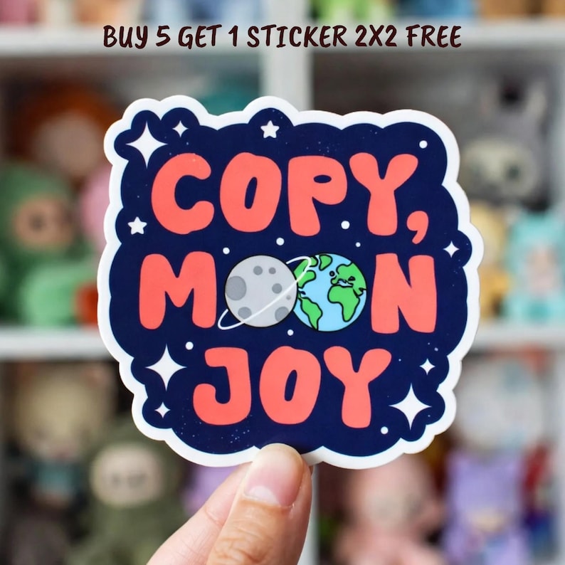 May include: A colorful sticker with the words "COPY, MOON, JOY" in red, with a moon and earth graphic. The sticker has a dark blue border with white stars. The text "BUY 5 GET 1 STICKER 2X2 FREE" is at the top.