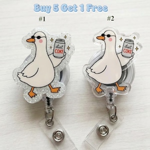 Peut inclure: Deux enrouleurs de badge représentant une oie blanche portant des lunettes de soleil noires et tenant une canette de soda étiquetée Diet Coke. Un enrouleur a une finition à paillettes argentées, l'autre est transparent. Texte Buy 5 Get 1 Free.