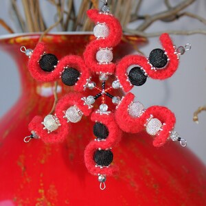 May include: A red and black snowflake ornament made of felt and beads. The snowflake is decorated with silver and black beads.