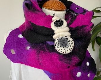 May include: A purple, black, and white felted wool scarf with a white beaded embellishment. The scarf is draped over a white shirt.