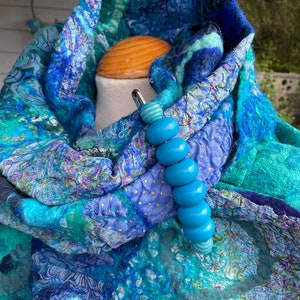 May include: A blue and green patterned scarf with a blue beaded scarf clip. The scarf is made of wool and has a textured surface.