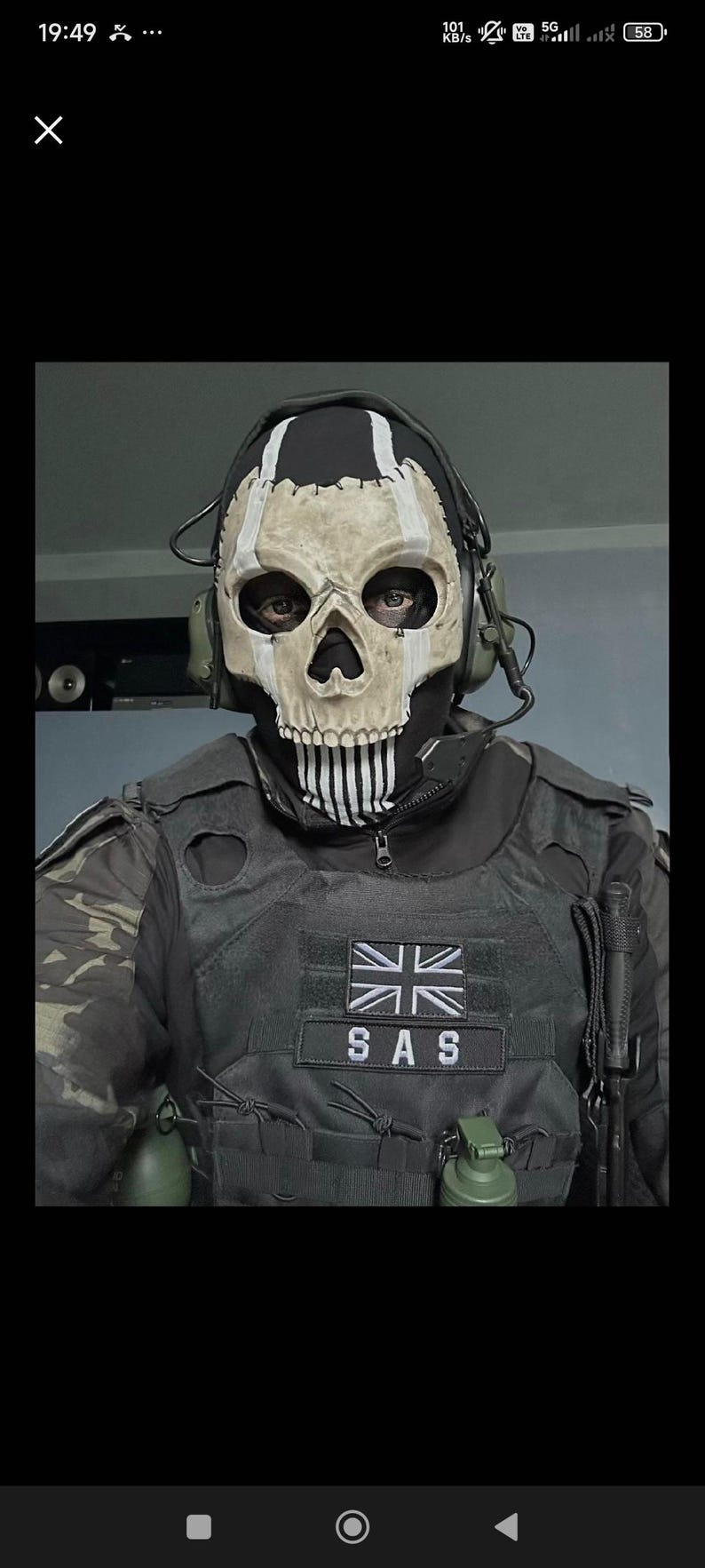 May include: A person wearing a skull mask with a black hood and a tactical vest. The mask is white with black details, resembling a skull. The vest has a patch with the Union Jack and the letters "SAS".