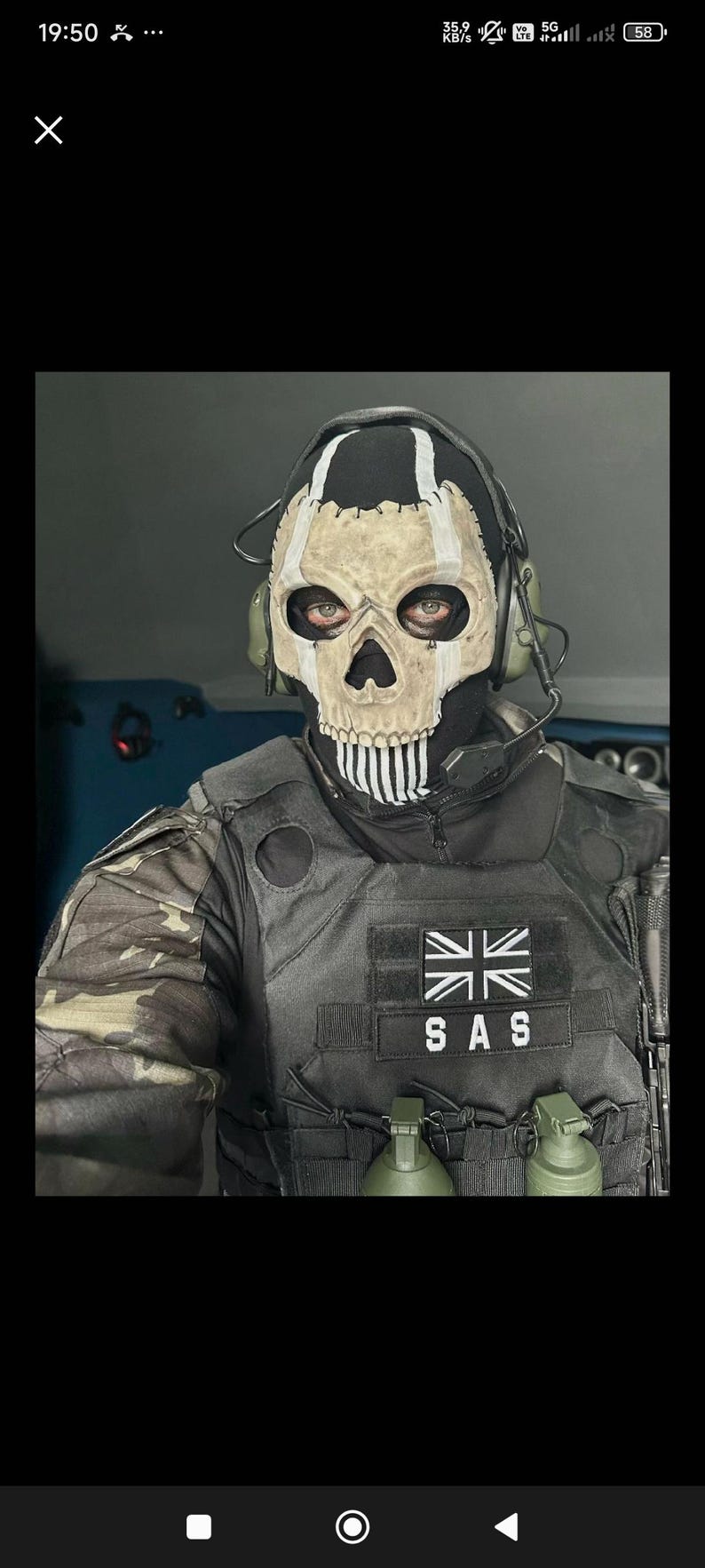 May include: A person wearing a skull mask with a black hood and tactical vest. The mask has a white skull design with black accents. The vest has a Union Jack patch and the letters "SAS". Two green grenades are attached to the vest.