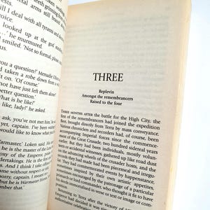 Puede incluir: Libro abierto con texto en p&aacute;ginas amarillentas. El t&iacute;tulo del cap&iacute;tulo "THREE" es visible, junto con los subt&iacute;tulos "Replevin", "Amongst the remembrancers" y "Raised to the four". El texto es de una novela.