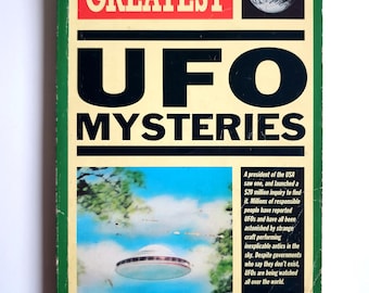 Puede incluir: Una portada de libro vintage titulada "THE WORLD'S GREATEST UFO MYSTERIES". La portada presenta un diseño retro con texto en negrita, una imagen de un OVNI en el cielo y una imagen de la Tierra. El libro es de Roger Boar & Nigel Blundell.