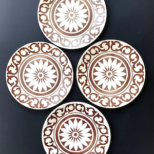 Puede incluir: Juego de cuatro platos de cena de cerámica blanca con un diseño floral marrón. Los platos tienen un borde elevado y un borde decorativo.