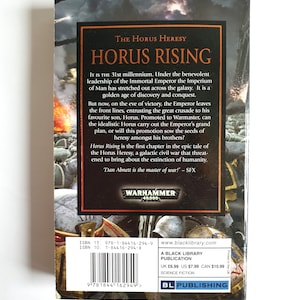 Puede incluir: La contraportada de "Horus Rising", una novela de ciencia ficci&oacute;n de la serie Warhammer 40,000. La portada presenta un fondo oscuro con texto en naranja y blanco, incluido el t&iacute;tulo y una sinopsis de la historia.