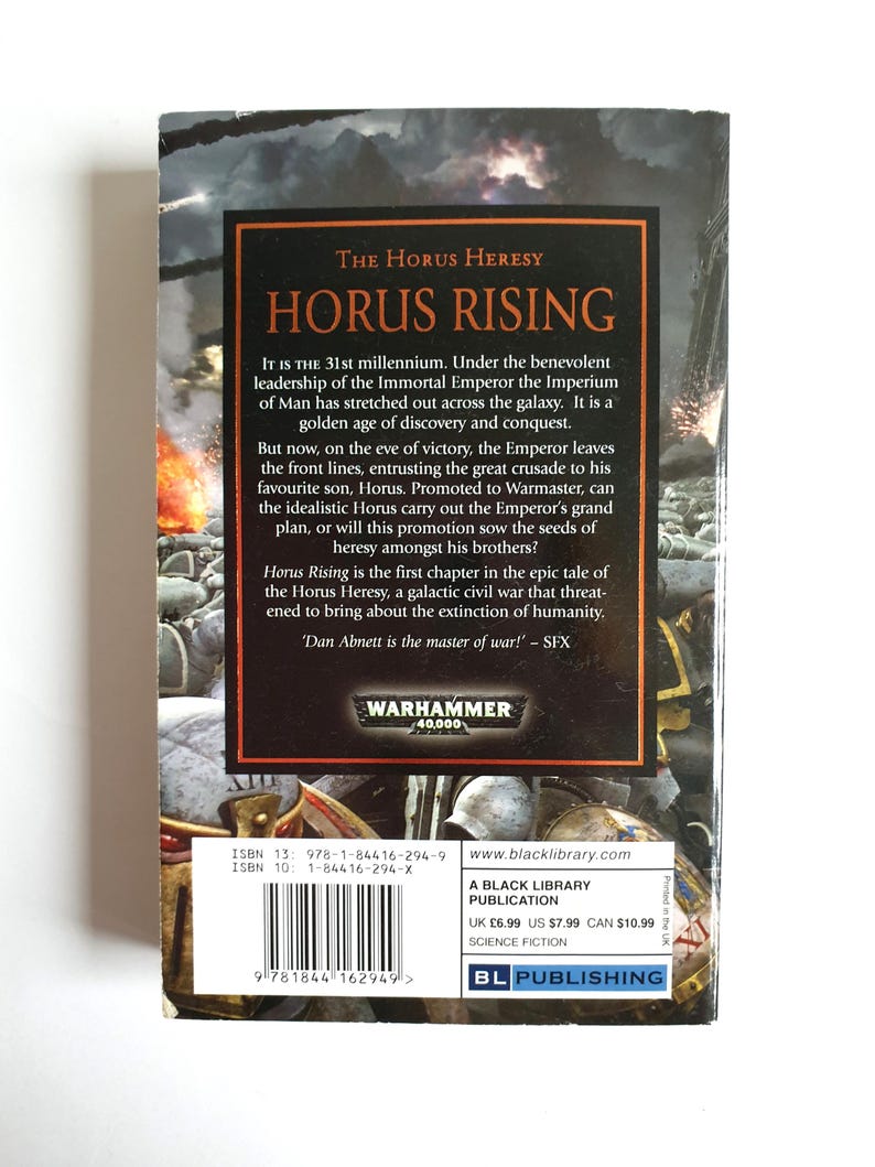 Puede incluir: La contraportada de "Horus Rising", una novela de ciencia ficci&oacute;n de la serie Warhammer 40,000. La portada presenta un fondo oscuro con texto en naranja y blanco, incluido el t&iacute;tulo y una sinopsis de la historia.